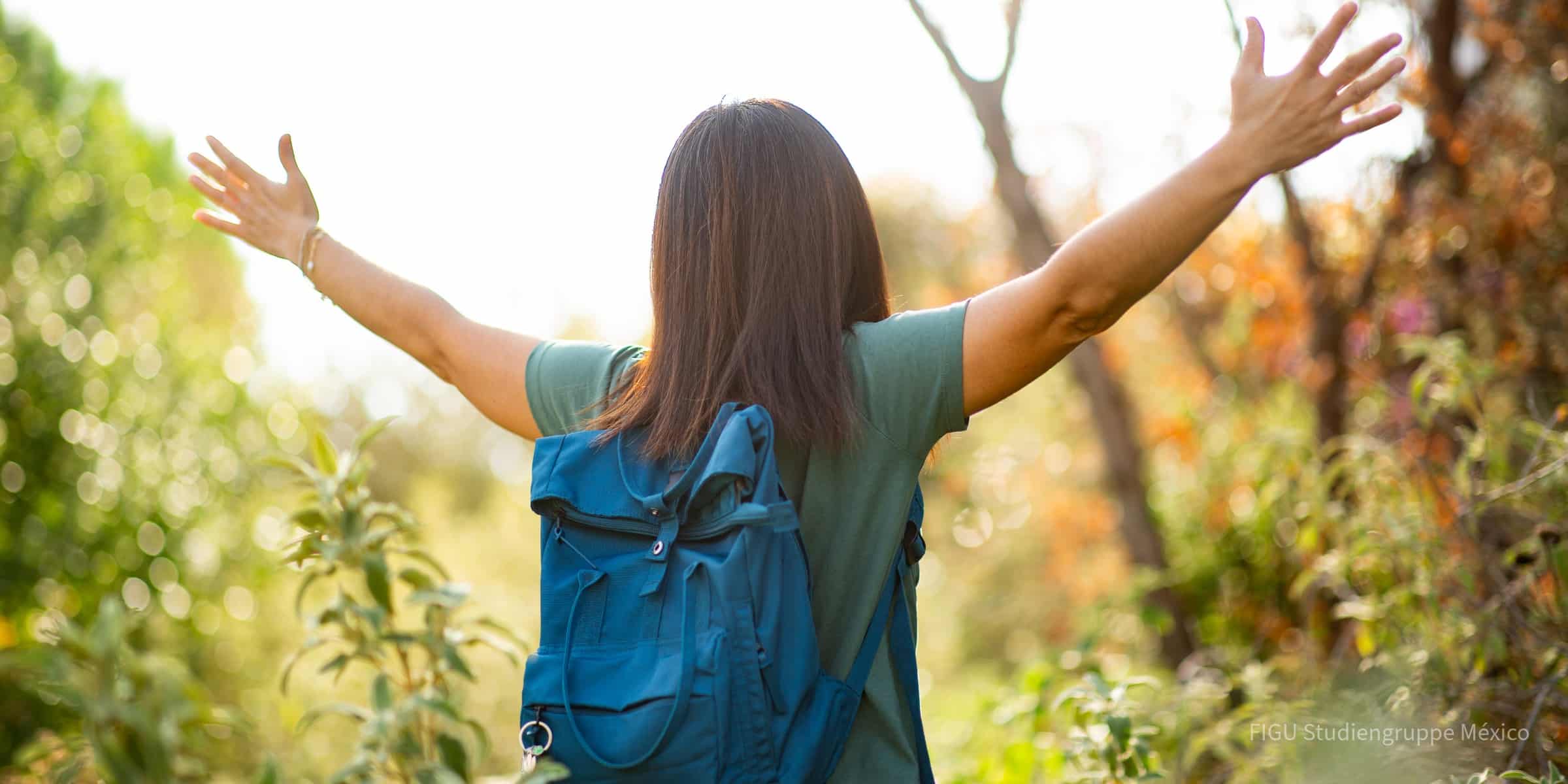 Senderista con mochila y brazos levantados en un sendero soleado.