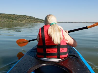 Persona de espaldas en kayak sobre un lago, con chaleco salvavidas rojo.
