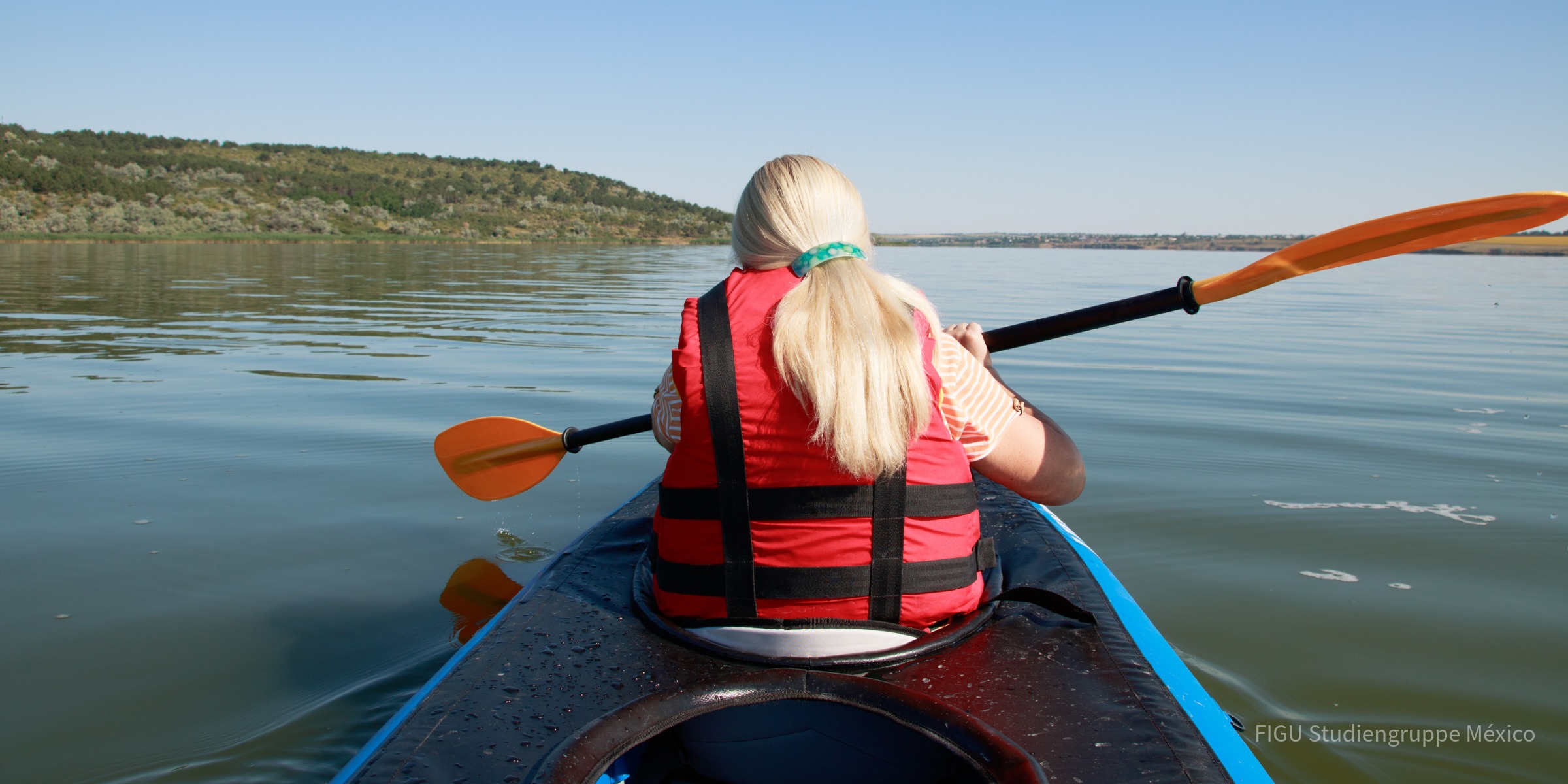 Persona de espaldas en kayak sobre un lago, con chaleco salvavidas rojo.