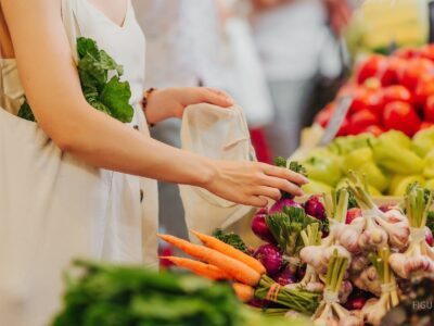 Manos colocando frutas y verduras en una bolsa de algodón en un mercado.