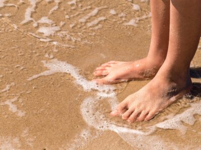 Pies descalzos en el agua junto a una playa de arena.