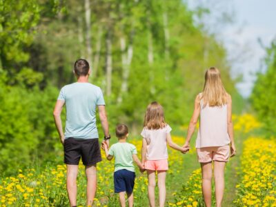 Familia de espaldas caminando de la mano por un sendero primaveral.