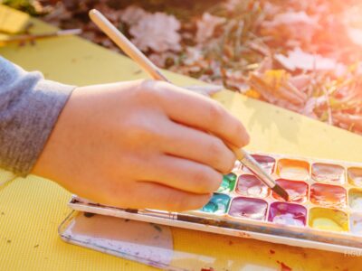 Manos con un pincel y pinturas de acuarela al aire libre.