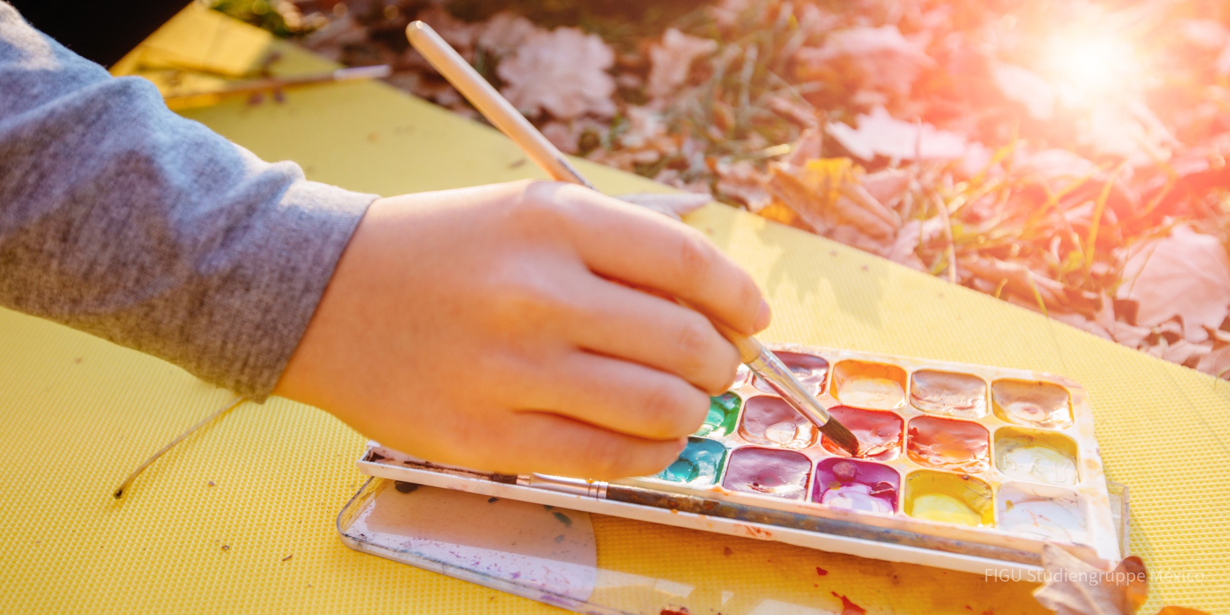 Manos con un pincel y pinturas de acuarela al aire libre.