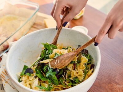 Manos mezclando una ensalada de pasta en un recipiente.