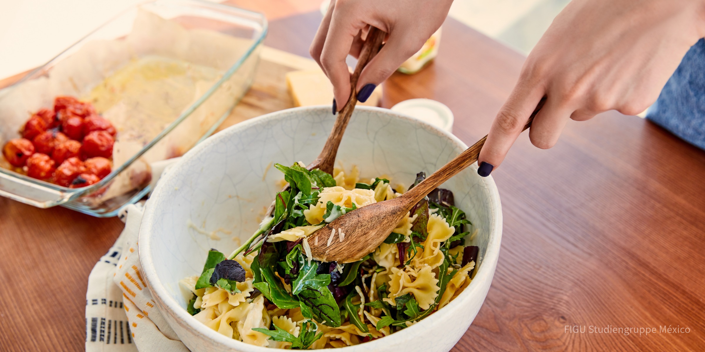 Manos mezclando una ensalada de pasta en un recipiente.
