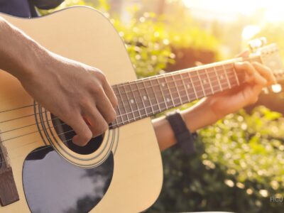 Mano tocando una guitarra en un parque iluminado por el sol.