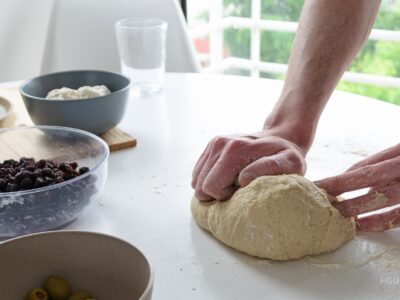 Manos amasando pan casero sobre una mesa con ingredientes.