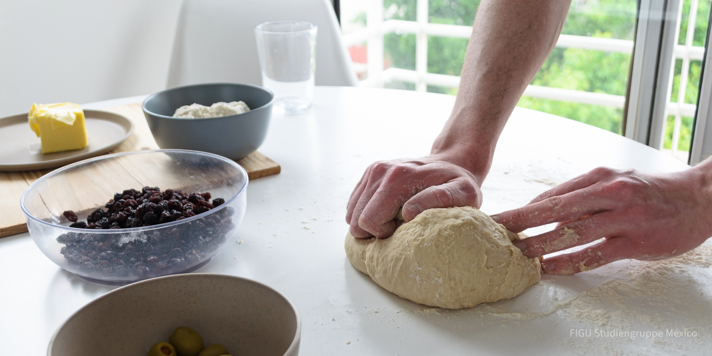 Manos amasando pan casero sobre una mesa con ingredientes.