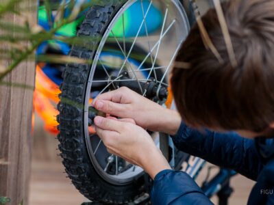 Manos de un niño inflando una llanta de bicicleta con una bomba roja.