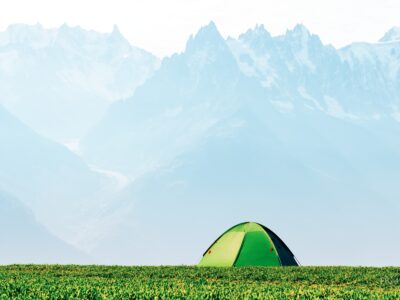 Tienda de campaña verde en una pradera de montaña durante el verano.