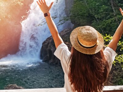 Persona con sombrero de paja y brazos levantados cerca de una cascada.
