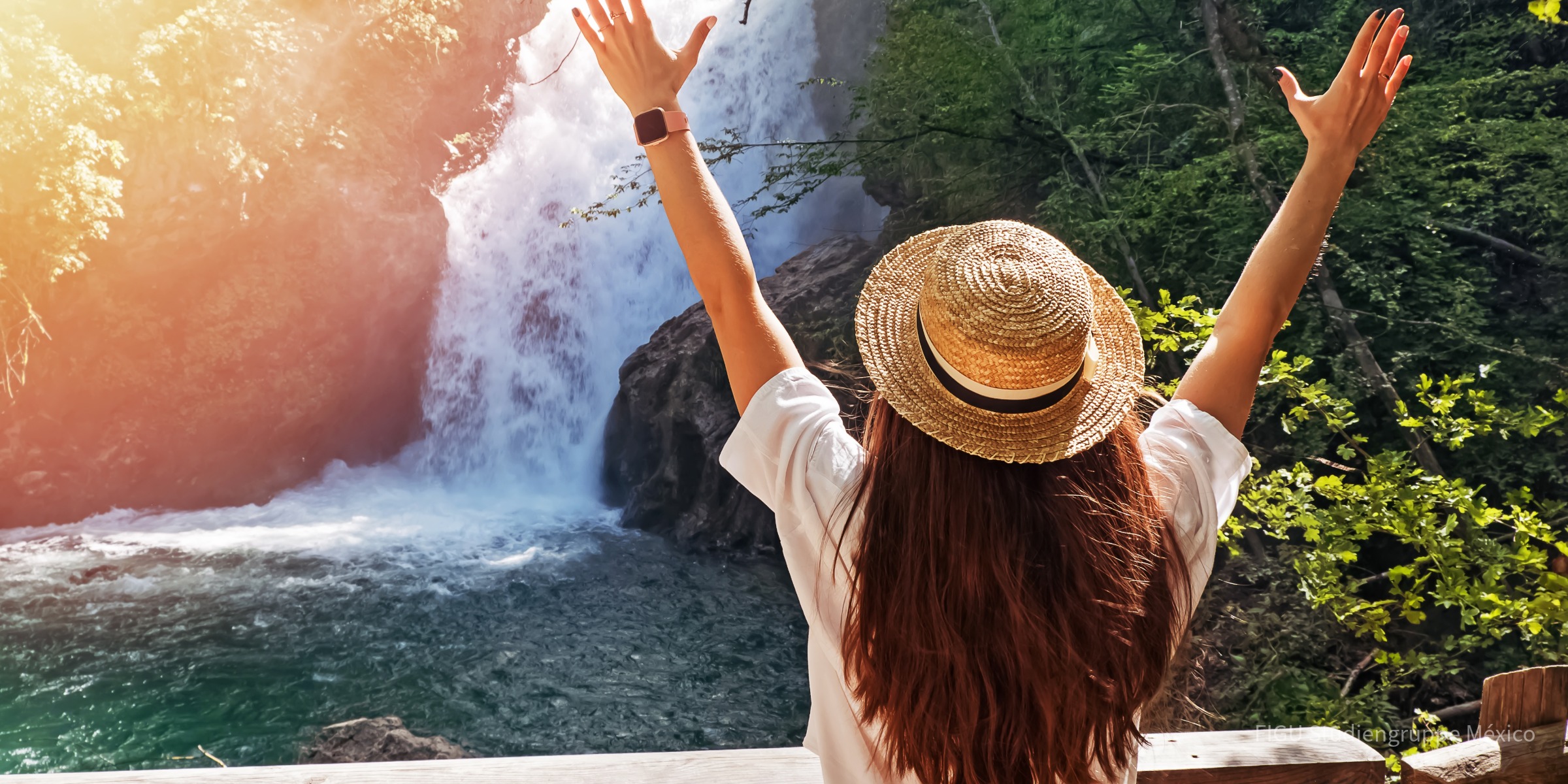 Persona con sombrero de paja y brazos levantados cerca de una cascada.